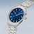 Herrenarmbanduhr mit rundem Gehäuse, blauem Zifferblatt und Metallarmband, Krone seitlich.
