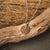"Collana con ciondolo rotondo in legno su catena d'argento appoggiata su un ramo di legno"