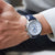Herrenarmbanduhr am Handgelenk: blaues Lederarmband, silbernes Gehäuse, weißes Zifferblatt