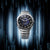 Herrenarmbanduhr mit blauem Akzent-Zifferblatt, rundes silbernes Gehäuse und Metallarmband.