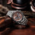 Herrenarmbanduhr seitlich mit silberfarbenem Edelstahlarmband und braunem Chronograph-Zifferblatt.