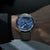 Alt text: Orologio Naos con quadrante a fasi lunari, cassa in acciaio inossidabile e cinturino in pelle nera.