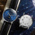 Alt text: Orologio Naos con quadrante a fasi lunari, cassa in acciaio inossidabile e cinturino in pelle marrone.