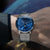 Alt text: Orologio Naos con quadrante a fasi lunari, cassa in acciaio inossidabile e cinturino in pelle marrone.
