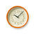 Runde Wanduhr mit orangem Rahmen, beigem Zifferblatt und schwarzen Zeigern