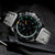 Orologio da uomo con quadrante nero, cassa argentata e cinturino in pelle nera.