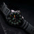 Orologio da uomo con quadrante nero, lancetta dei secondi rossa e indici luminescenti verdi.