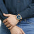Armbanduhr am Handgelenk mit blauem Zifferblatt, goldfarbener Lünette und dunkelblauem Armband