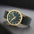 Unisex-Armbanduhr mit dunkelgrünem Zifferblatt, goldfarbenem Gehäuse und grauem Stoffband.