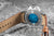 Orologio da uomo con cinturino in pelle marrone; logo blu visibile sul fondello.