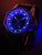 Orologio da uomo con quadrante scuro e indici luminescenti, cinturino nero, lunetta argentata.