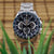 Silberne Herrenuhr mit blauem Zifferblatt und Metallarmband, sichtbare Knöpfe