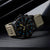 Herrenuhr mit beigem Armband und schwarzem Zifferblatt, Leuchtmarkierungen in Blau