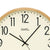 Quadrante dell'orologio da parete nel dettaglio: quadrante beige, numeri 12 e lancette neri, bordo in legno chiaro.