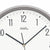 Funk-Wanduhr Nahansicht: weißes Zifferblatt mit AMS-Logo, schwarzen Zeigern und goldener Achse