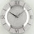 Nahaufnahme Wanduhr: silberner Ring, römische Zahlen, Logo „AMS.” und Zeiger
