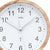 Nahaufnahme: Wanduhr mit Holzoptik-Rand, weißem Zifferblatt, AMS-Logo und Zeigern